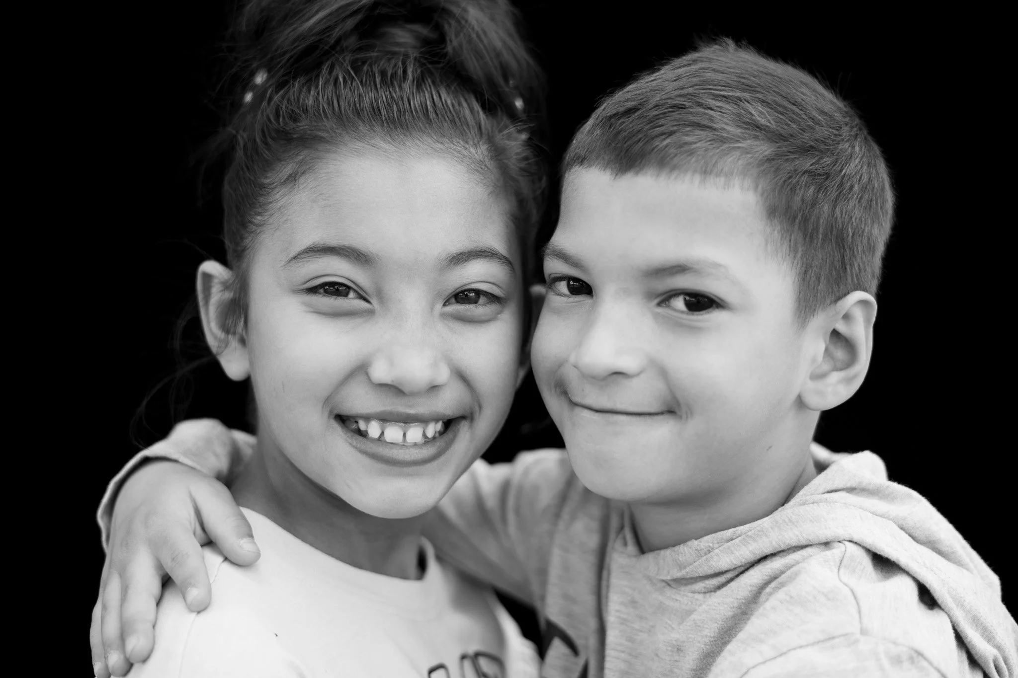 Two children, a girl and a boy, smiling and hugging each other, with a black background.