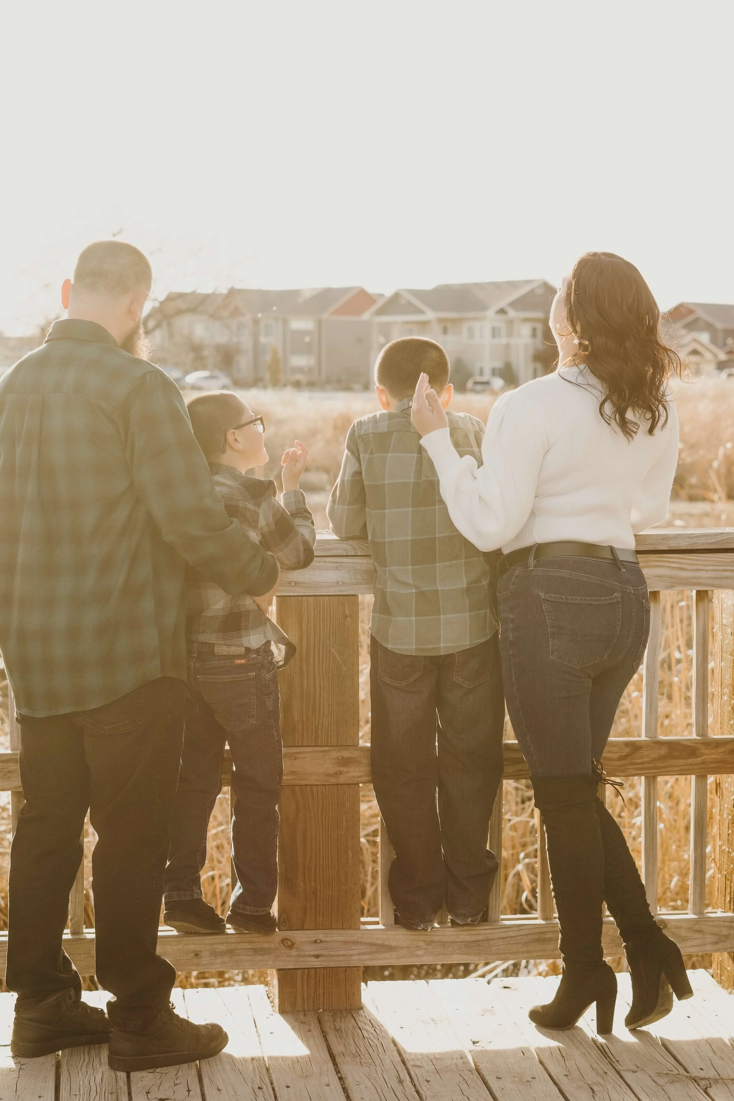 A family of five standing on a wooden deck, looking out at a suburban neighborhood with houses in the background during sunset.