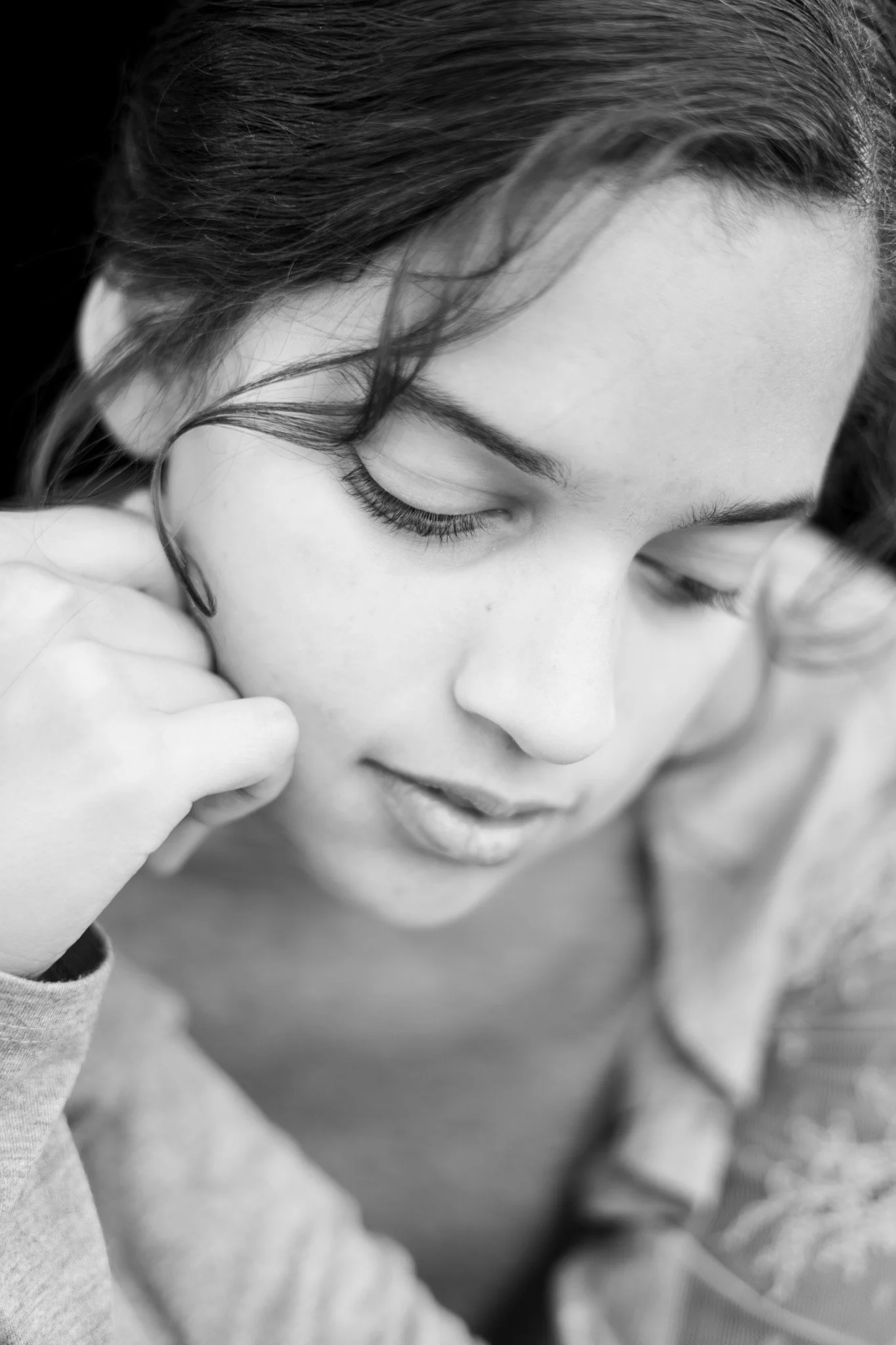Close-up black and white photo of a woman with her eyes closed, gently touching her face with her hand, with her hair falling across her face.