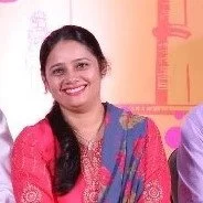 Swagatika smiling, wearing a pink and blue traditional outfit, sitting in front of a colorful background.