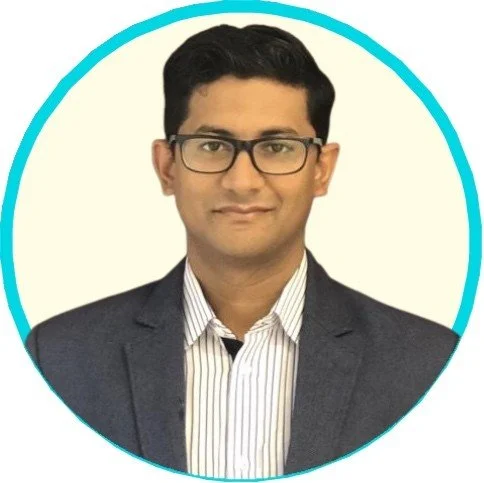 Anirban with short black hair, glasses, wearing a dark blazer and a white striped shirt, smiling in front of a plain light background with a blue border.