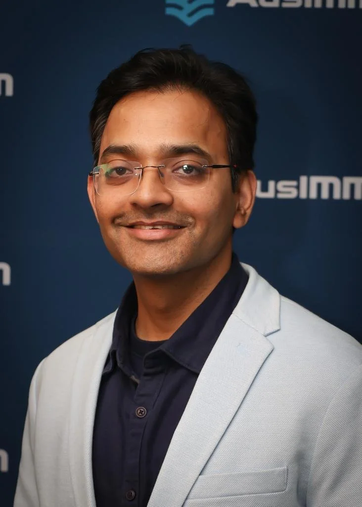 Sushant Dayal wearing a white blazer over a dark shirt, standing in front of a blue background with logos.