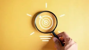 Hand holding magnifying glass over a target symbol on yellow background