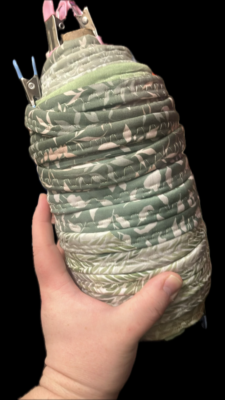 Hand holding a sage green floral quilted corded fabric bundle with clothespins attached to the top before the jelly roll rug is made