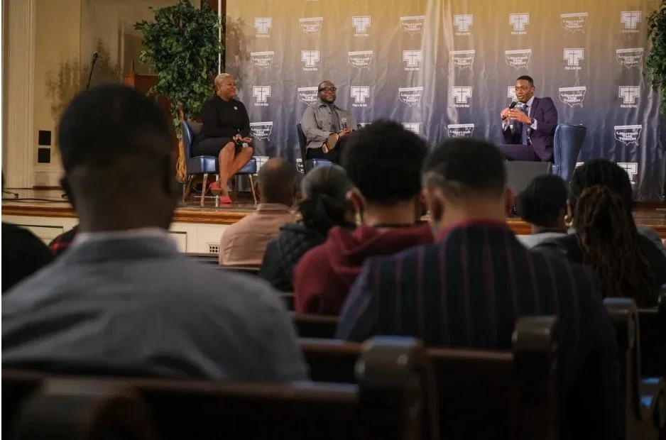 Panel discussion on stage with three speakers and audience in a conference room.