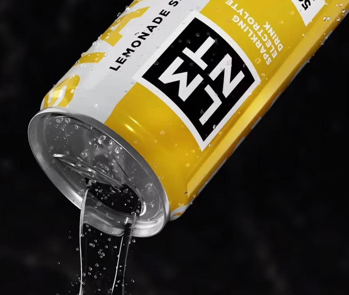 A LMNT yellow and white can of sparkling lemon soda with bubbles, tilted and pouring liquid into the air against a black background.