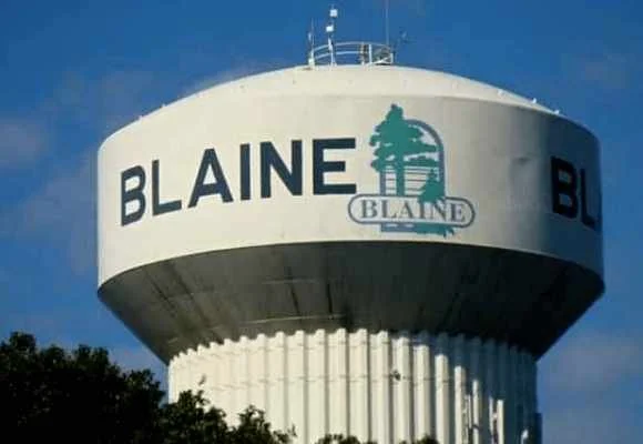 A large white water tower with the word 'BLAINE' and a logo featuring a tree on it, set against a blue sky.
