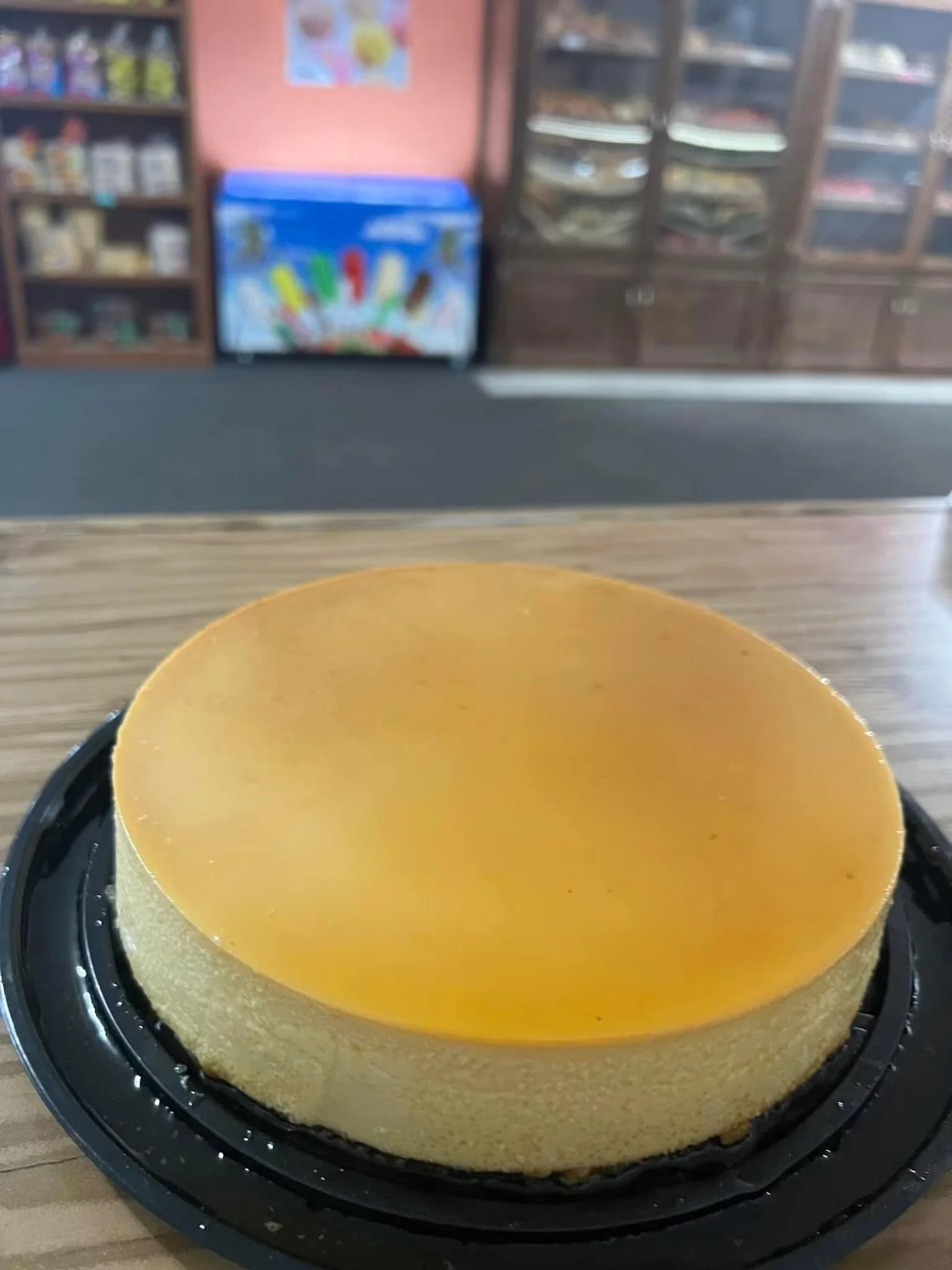 Close-up of a plain, unbaked, yellow cheesecake in a round pan on a wooden surface.