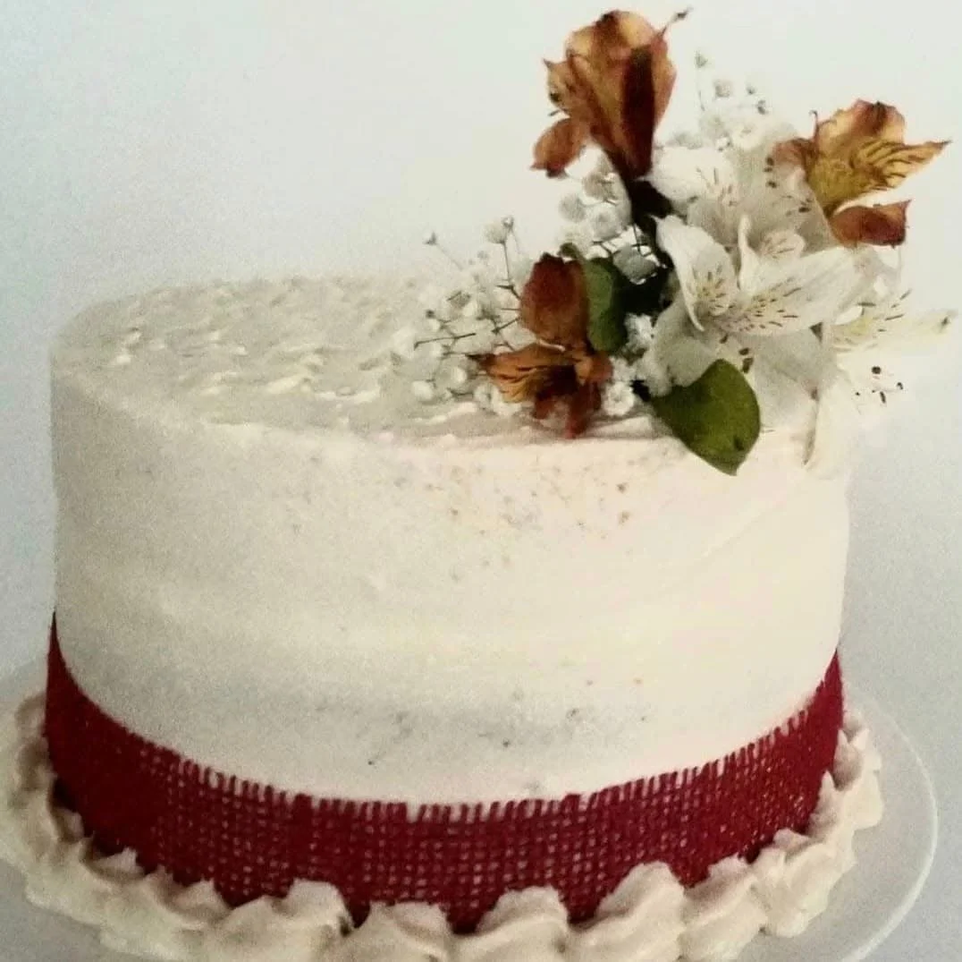 A round white cake decorated with dried flowers on top and a red ribbon around the bottom edge.