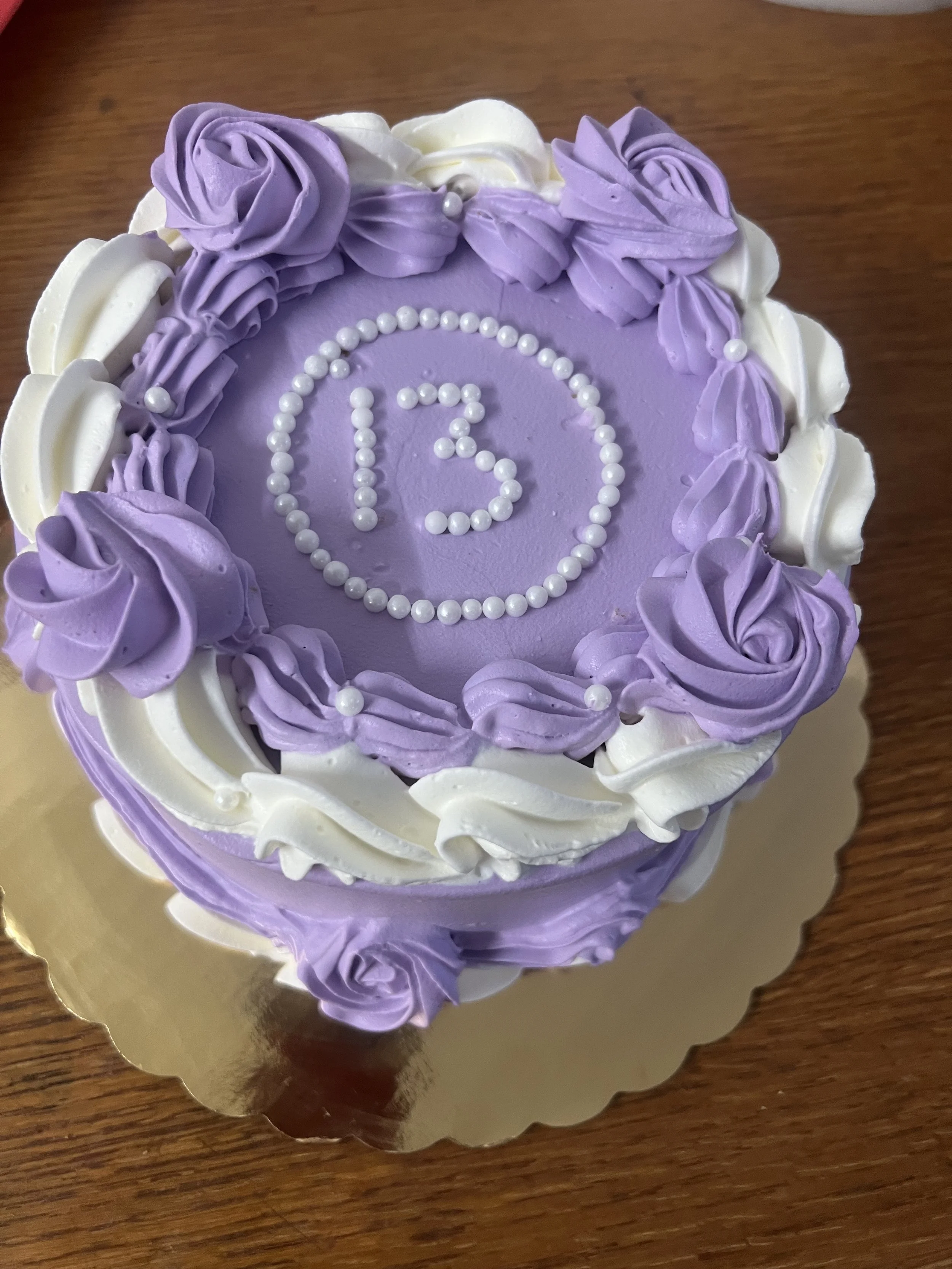 A birthday cake with purple and white frosting, decorated with the number 13 in white pearl-like decorations at the center.