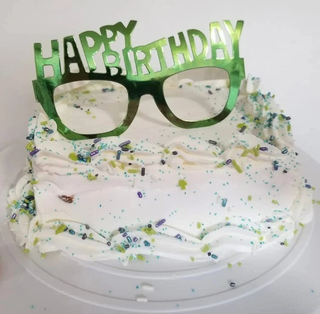A birthday cake with white frosting, decorated with colorful sprinkles, and topped with a green 