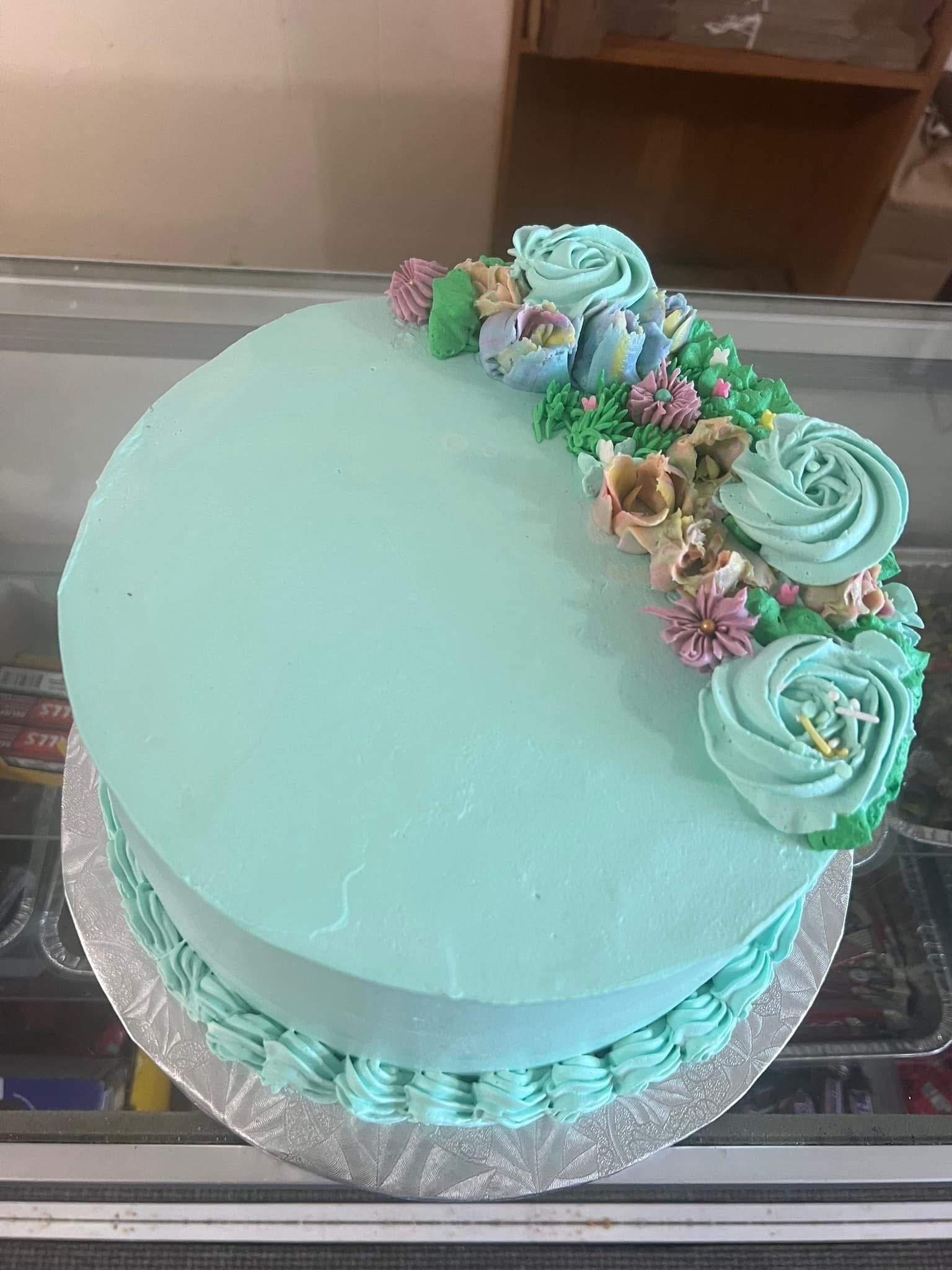 Mint green frosted cake decorated with pastel-colored icing flowers on top and piped border around the sides.