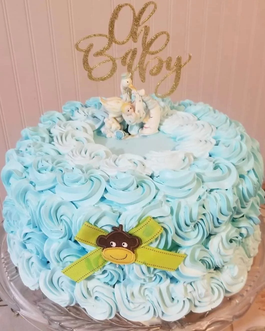 Baby shower cake decorated with blue and white rosette frosting, a fondant unicorn and 'Oh Baby' glittery topper, with a cute monkey and the baby shower theme.