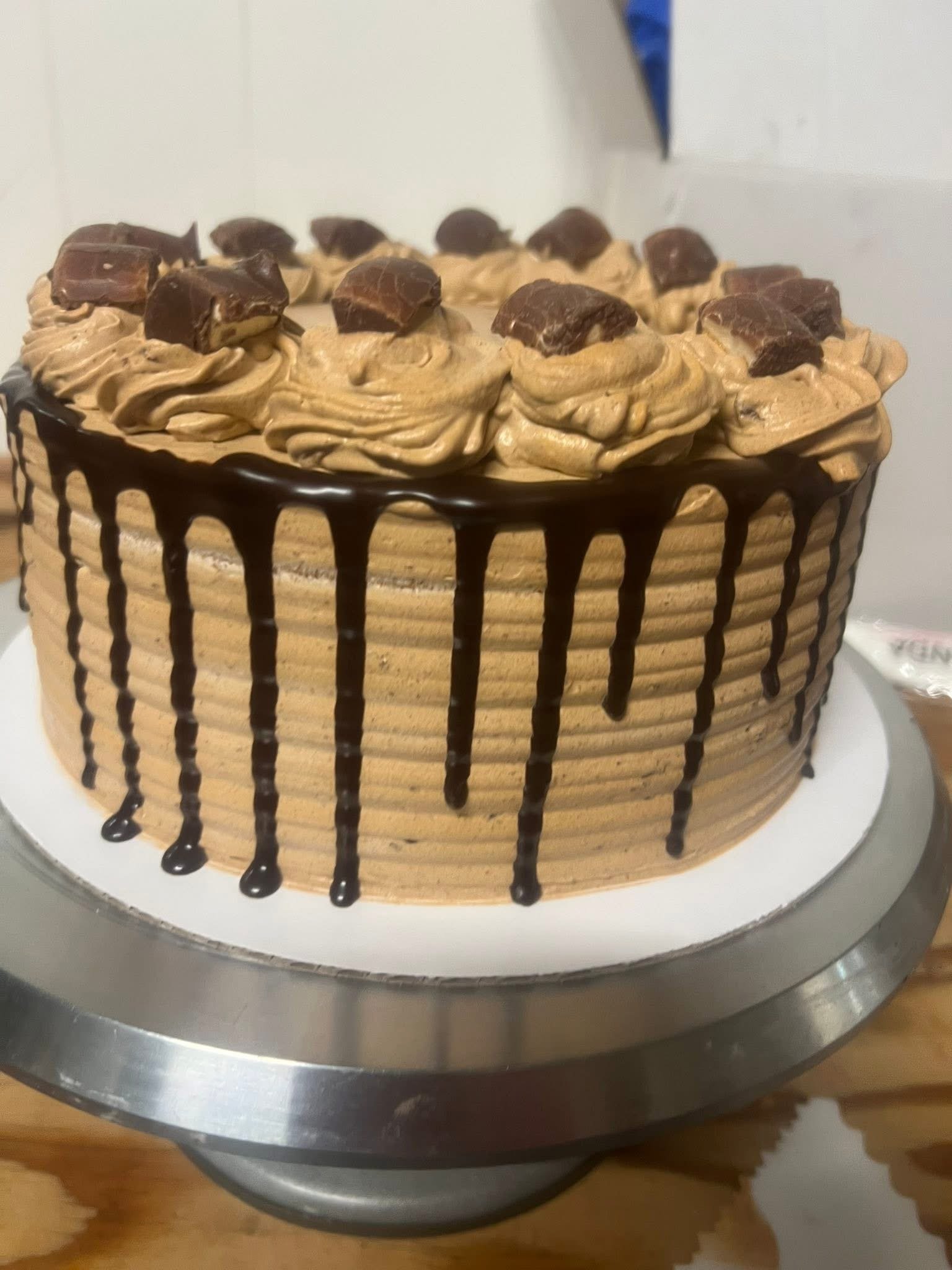 Chocolate cake with swirled frosting, topped with pieces of chocolate and drizzled with chocolate sauce around the side.