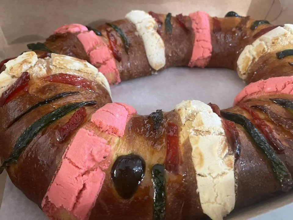A circular bread wreath decorated with pink and white marshmallows, and drizzled with chocolate and colorful icing.
