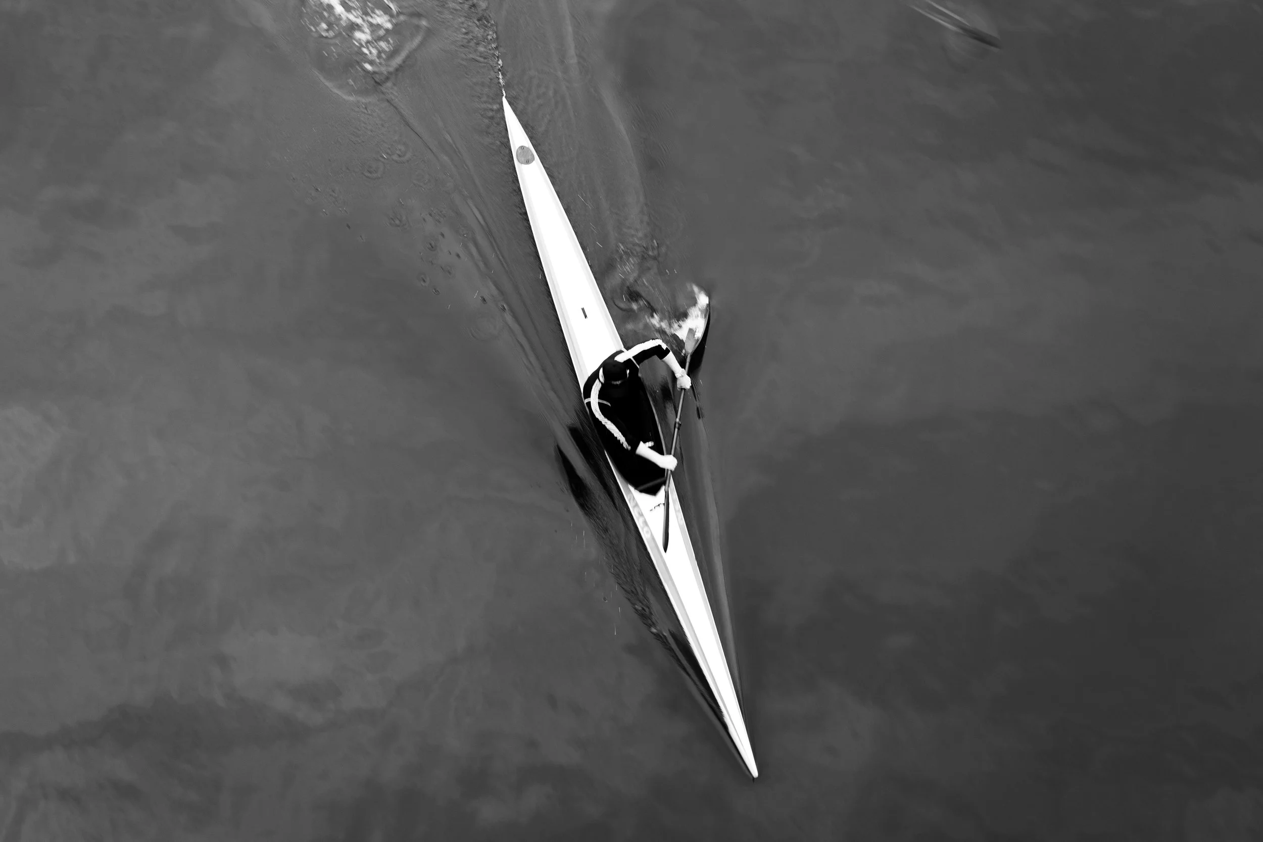 A person in a kayak paddling on water, viewed from above.