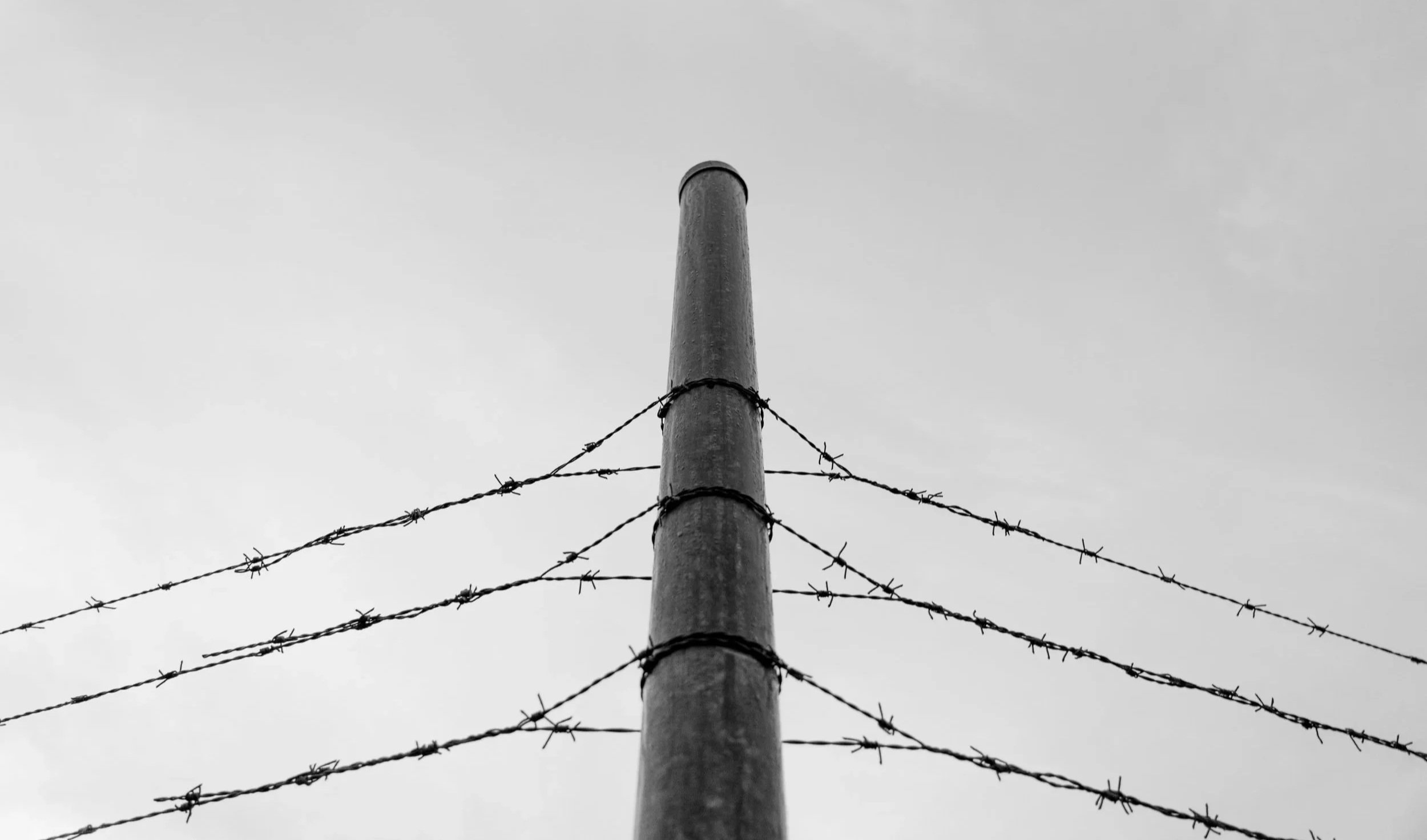 A black and white photo of a tall wooden pole with barbed wire fencing.