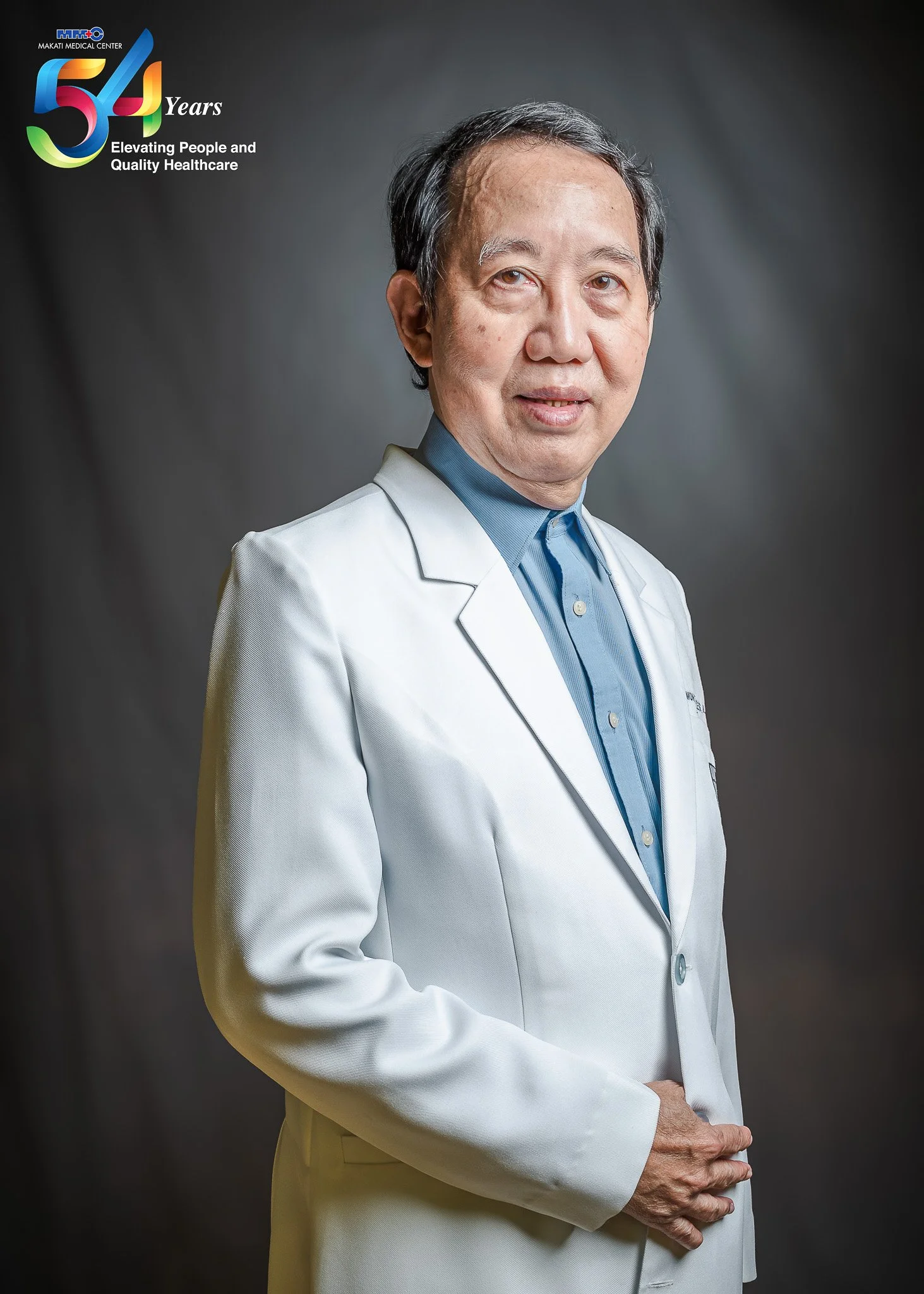 A male doctor in a white coat, standing with a gray background, with the Makati Medical Center 54th anniversary logo in the top left corner.