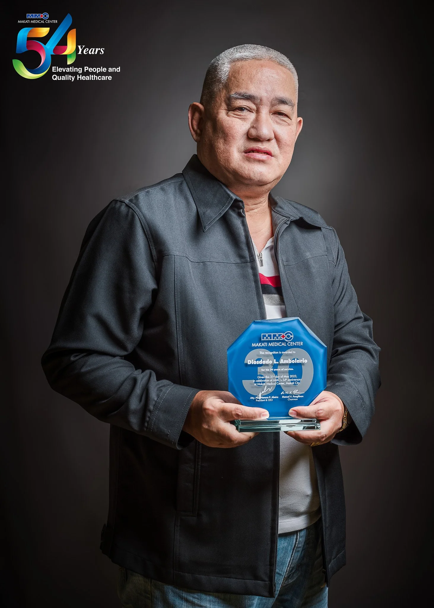 A man holding a blue award plaque from Makati Medical Center, standing against a dark background with a logo and the text '54 Years Elevating People and Quality Healthcare' at the top left.