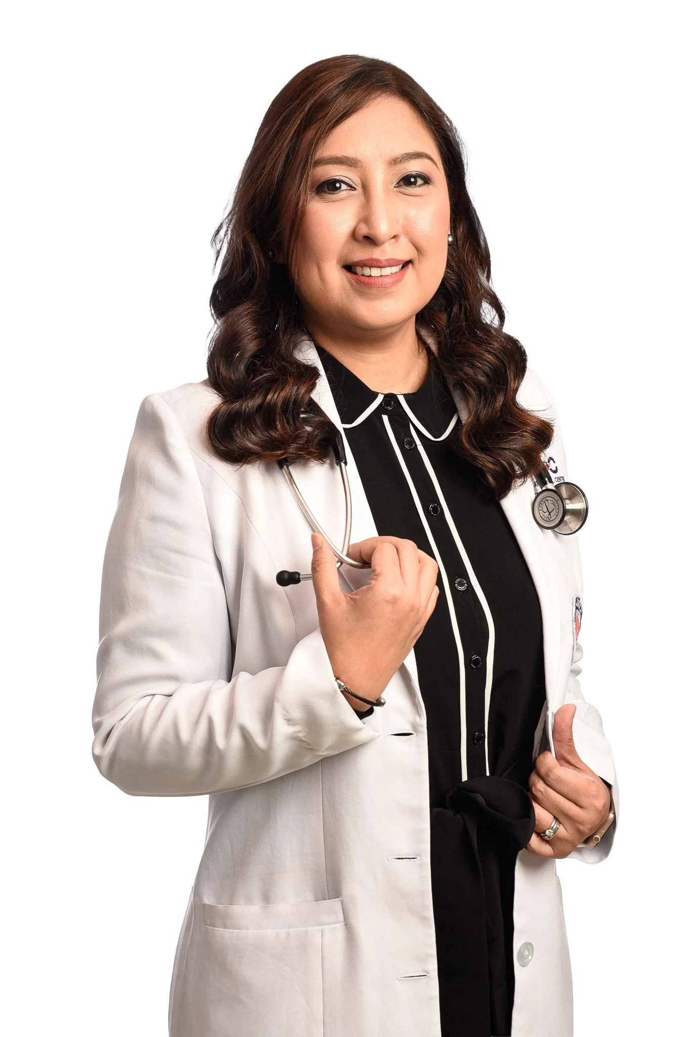 A female doctor with dark hair styled in loose curls, wearing a white lab coat over a black blouse with white piping, and holding a stethoscope.