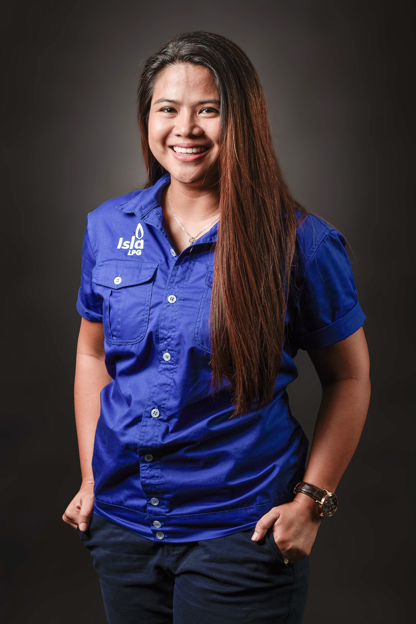 Portrait of a smiling woman with long brown hair wearing a blue shirt with 'Island LPG' logo, standing against a dark background.
