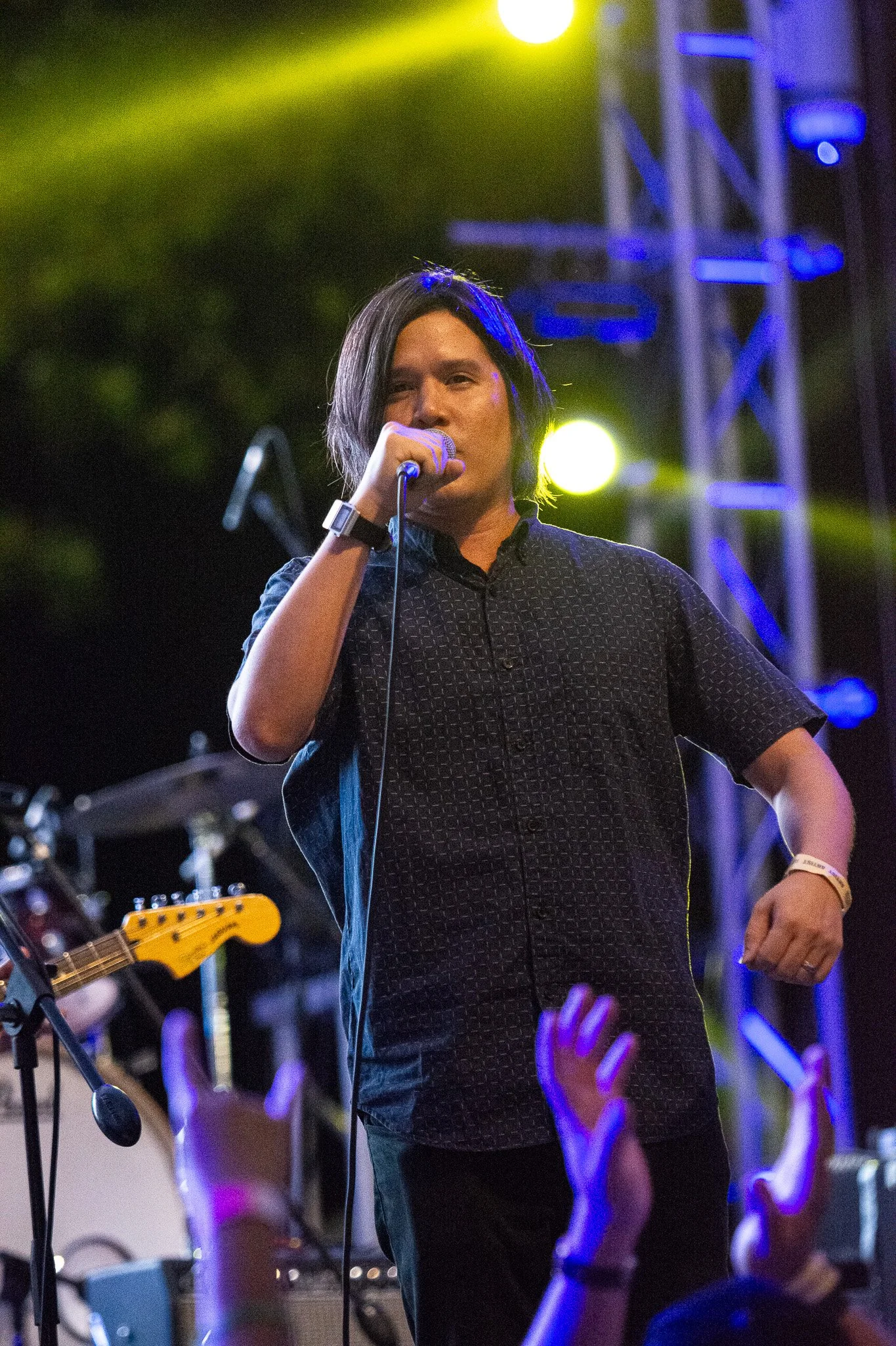 Male singer performing on stage with yellow and purple lights in the background, audience reaching out with hands.