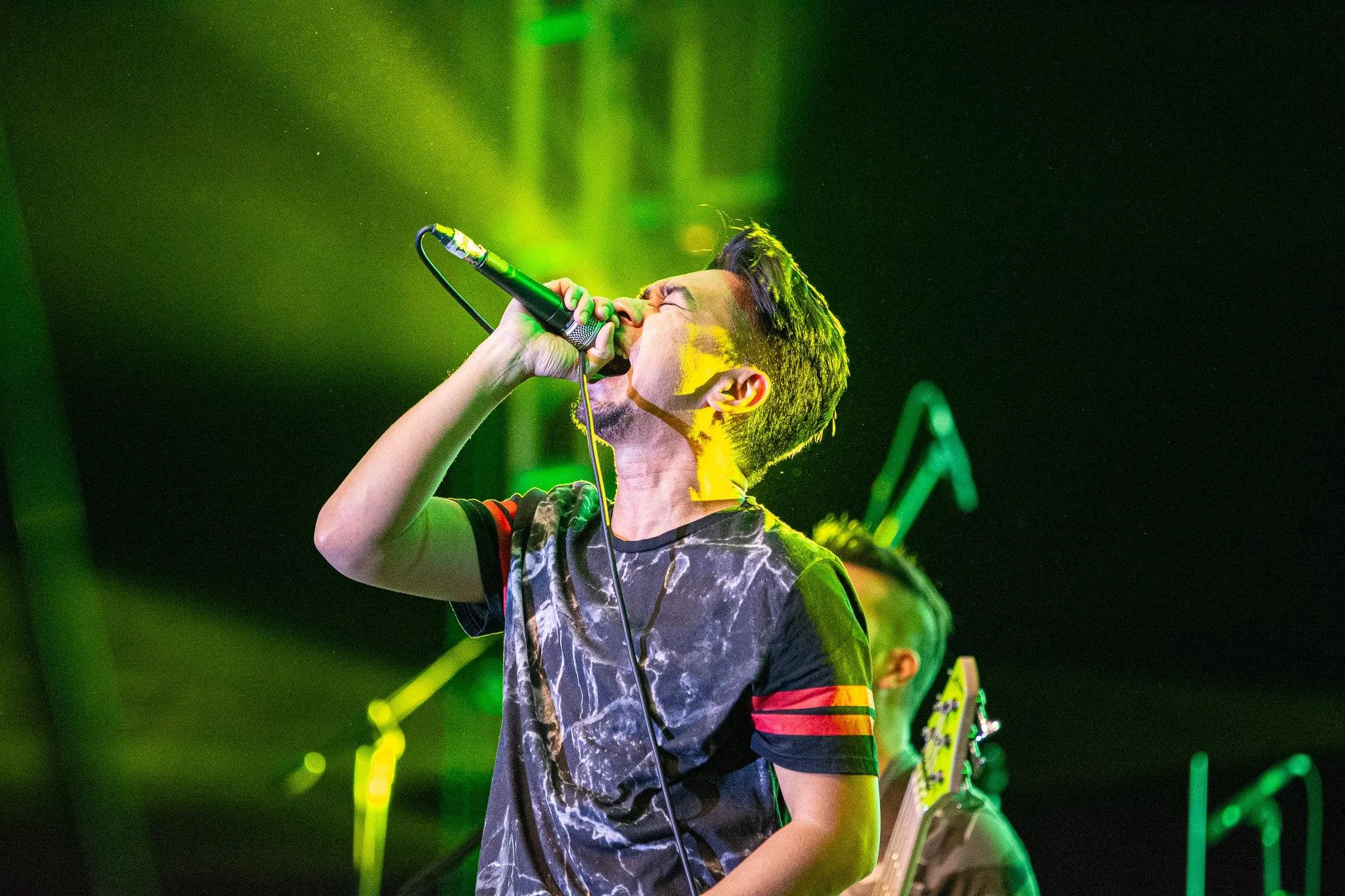 Young male singer passionately singing into a microphone on stage with green and yellow stage lighting
