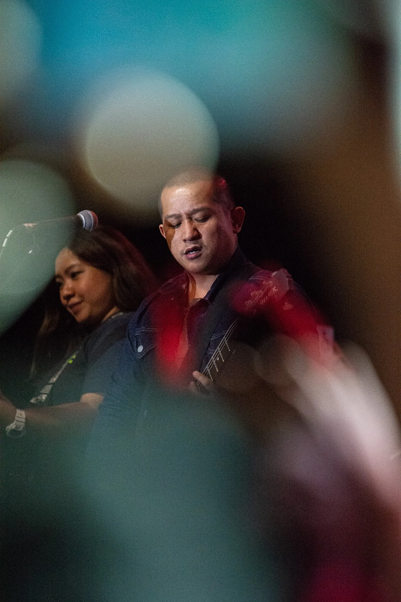 Two musicians performing on stage, with the focus on a man playing guitar and singing, accompanied by a woman.”}