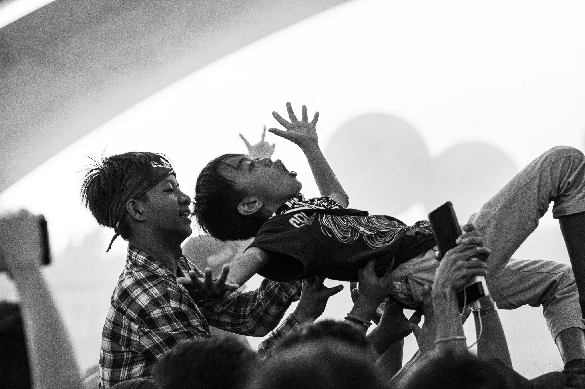 Black and white photo of children crowd surfing, with one child on top reaching upward and others holding the child from below.