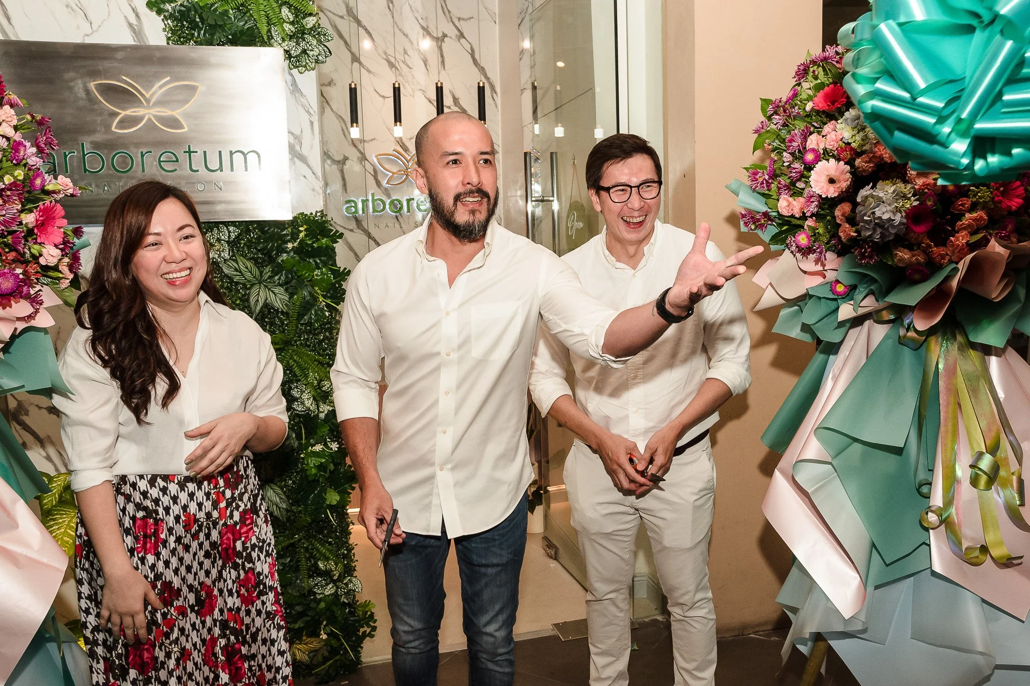 Four people standing in front of a floral display and a sign that reads 'arboritum.' Two men and two women, smiling and engaging in conversation at an event.