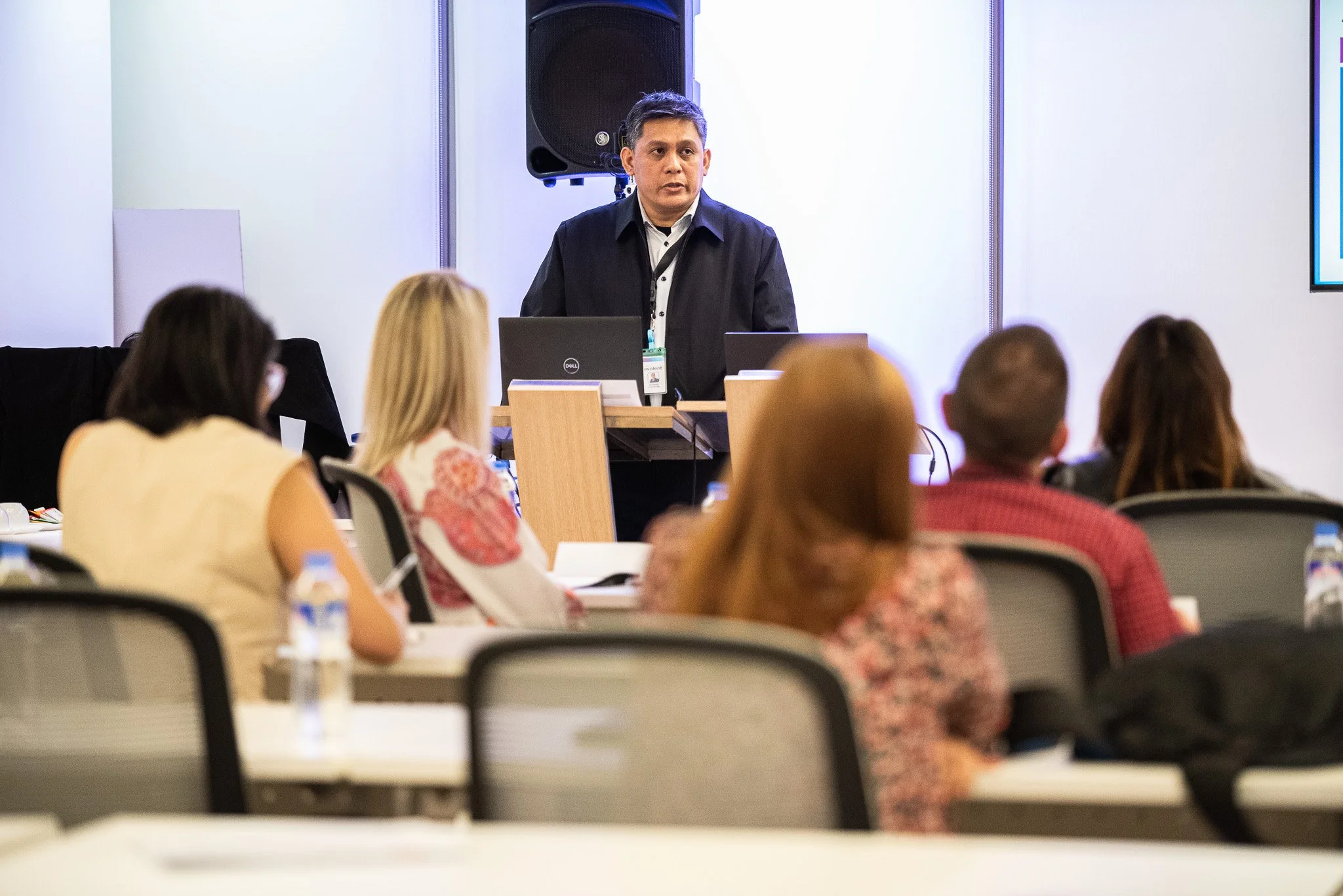 A man giving a presentation at a conference with attendees seated in front of him.