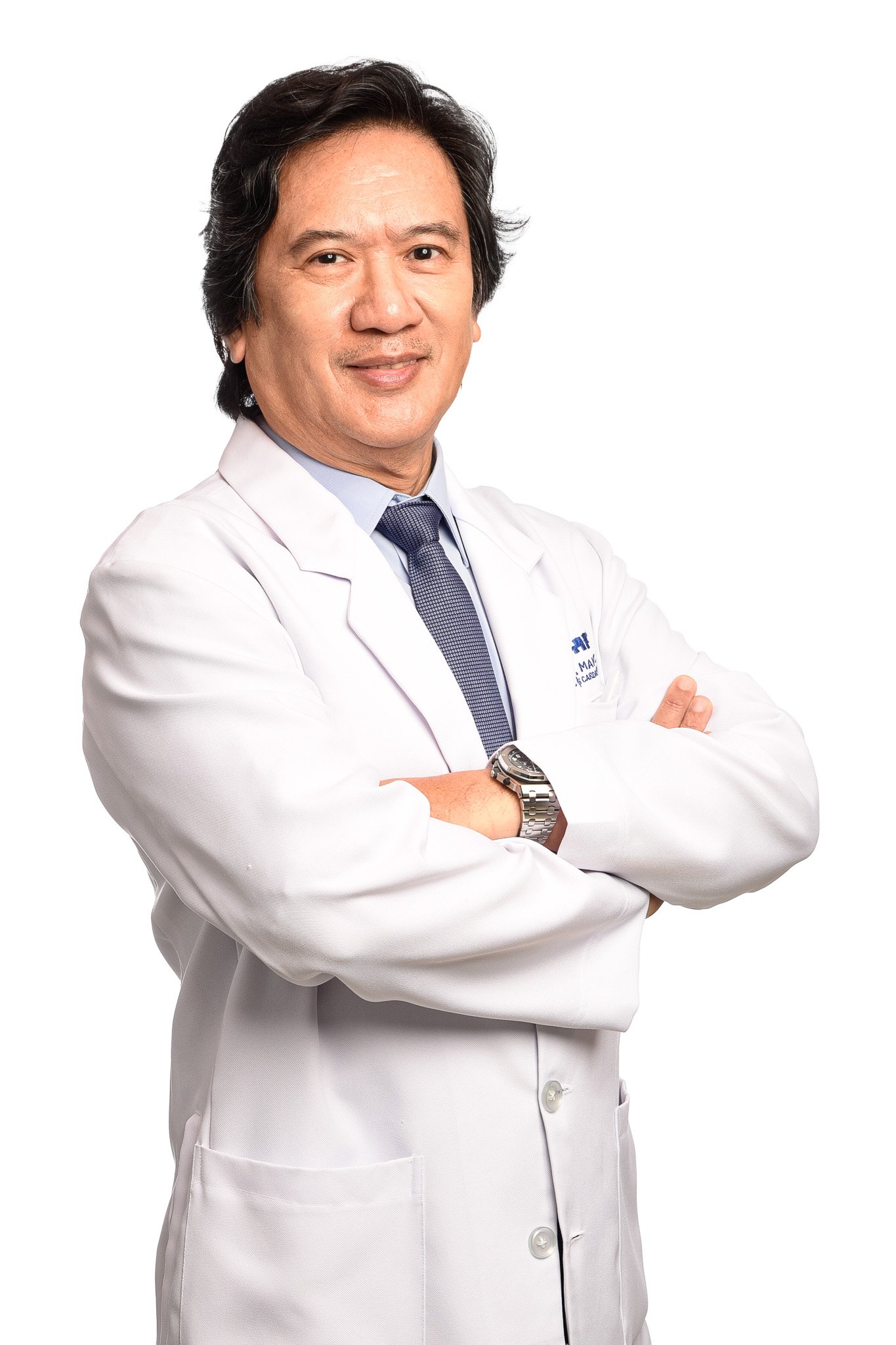 A male doctor with dark hair wearing a white lab coat, a light blue shirt, and a dark blue tie, standing with his arms crossed and smiling at the camera.