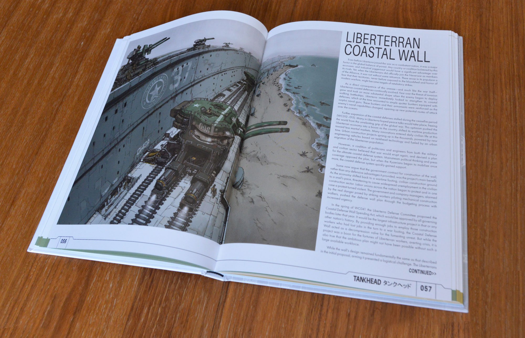 Open illustrated book about the Liberterranean Coastal Wall, showing a detailed drawing of a military tank on tracks next to the wall, with the sea and beach in the background, on a wooden surface.
The book is TANKHEAD Mechanical Encyclopedia.
