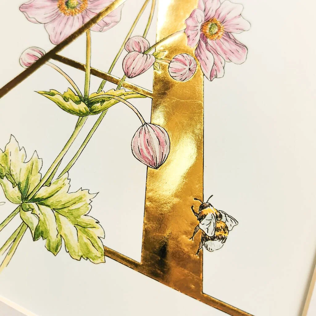 Watercolor illustration of pink flowers, green leaves, a golden rectangular frame, and a bee.
