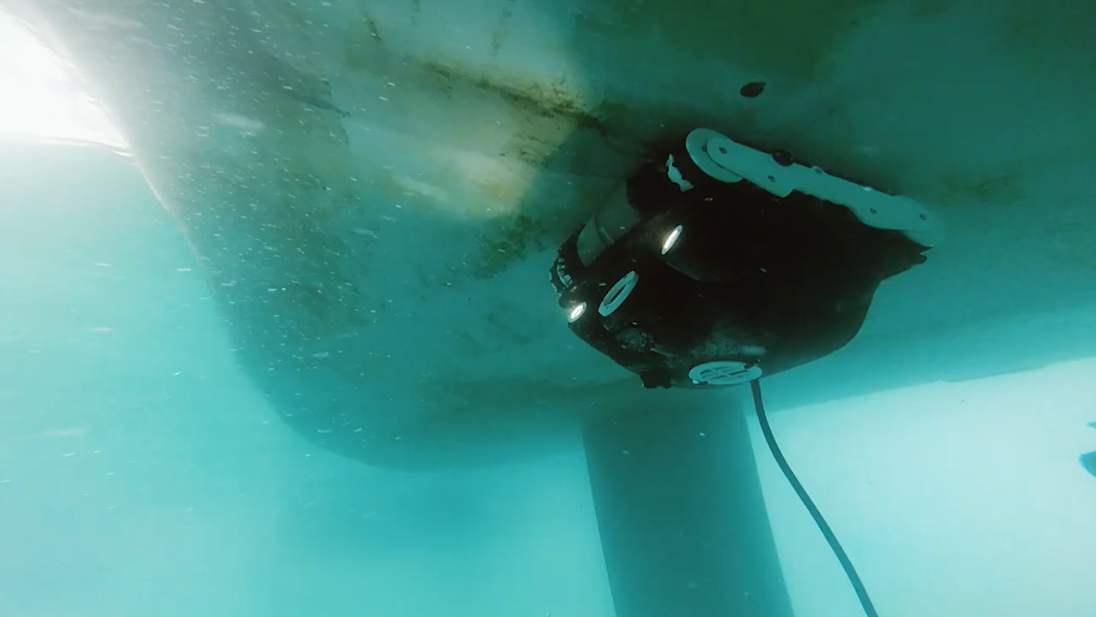 Underwater view of an underwater drone performing a hull clean beneath a boat in Auckland