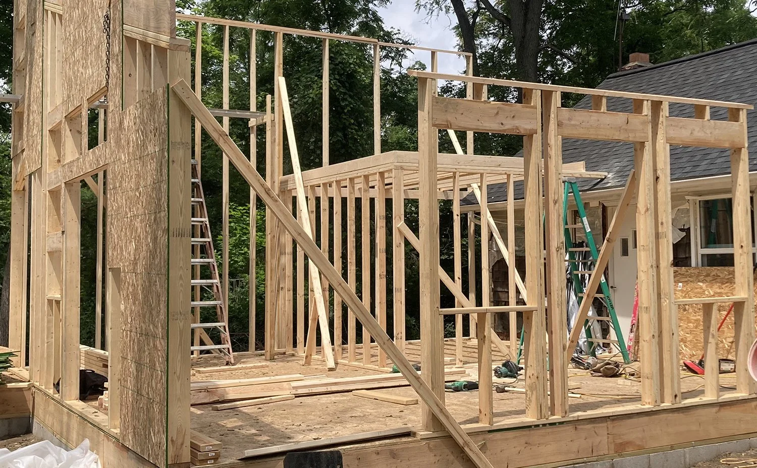 Wooden framing for a house under construction in a backyard, with ladders and construction tools visible.