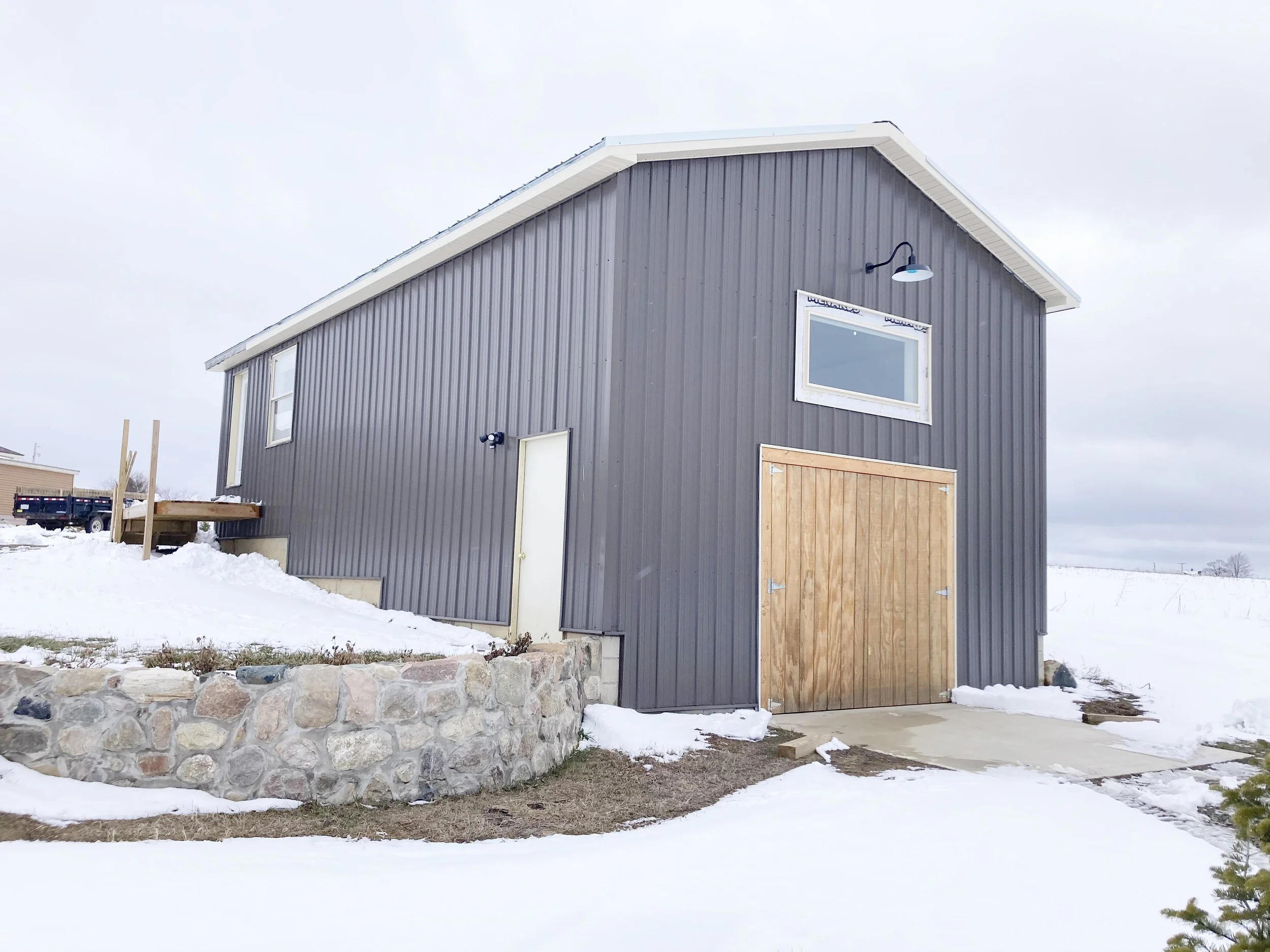 A small modern gray barn with a wooden sliding door on a snow-covered landscape.