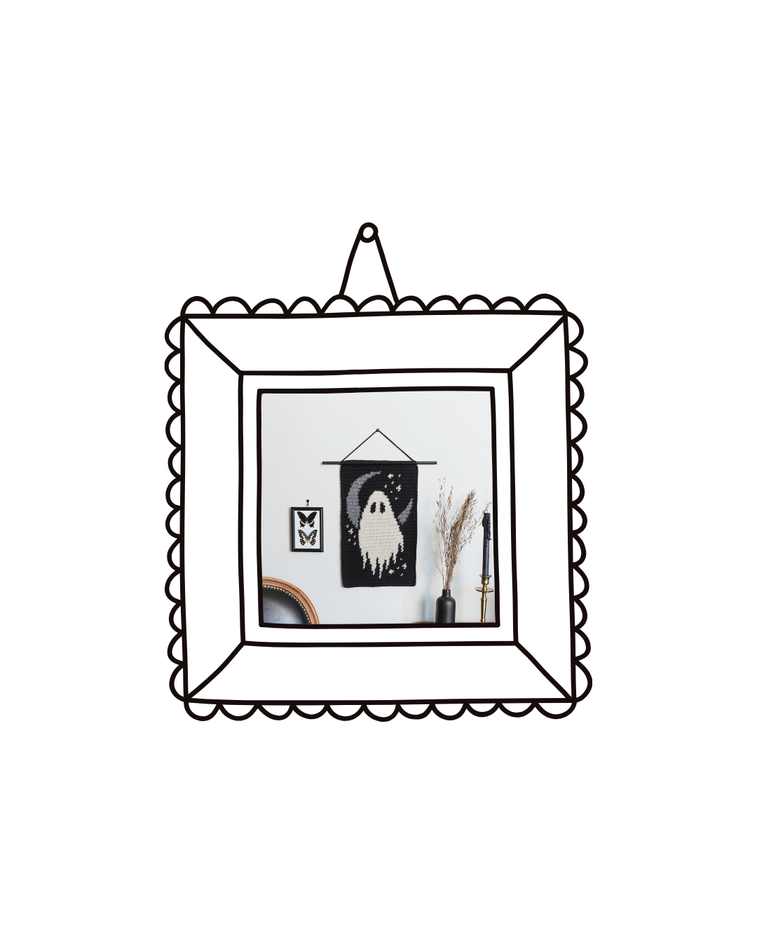 Decorative wall hanging of a ghost with a moon and stars, framed butterfly print, dried grass in a black vase, and a tall candle in a gold holder on a white wall.