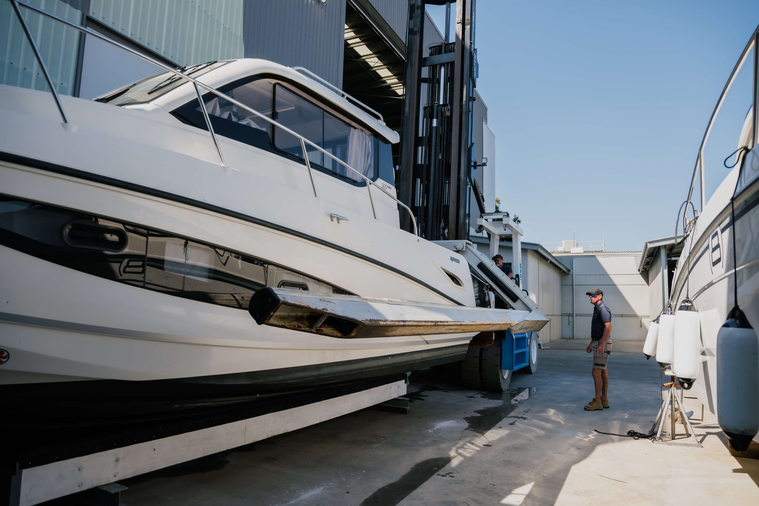 A photo of a boat in a marina storage area with a man in a cap and boots standing next to it.
