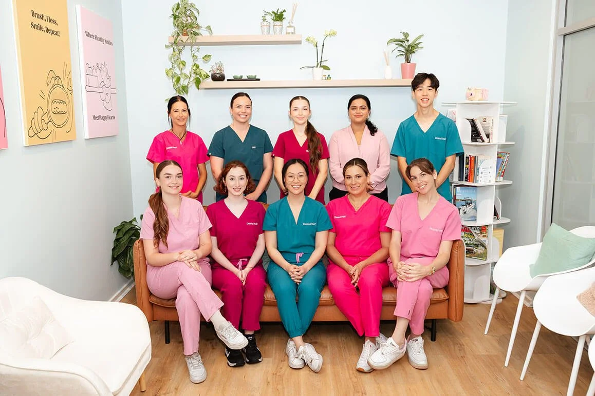 A dental team in pink and teal scrubs sitting on a lounge in a dental waiting room.