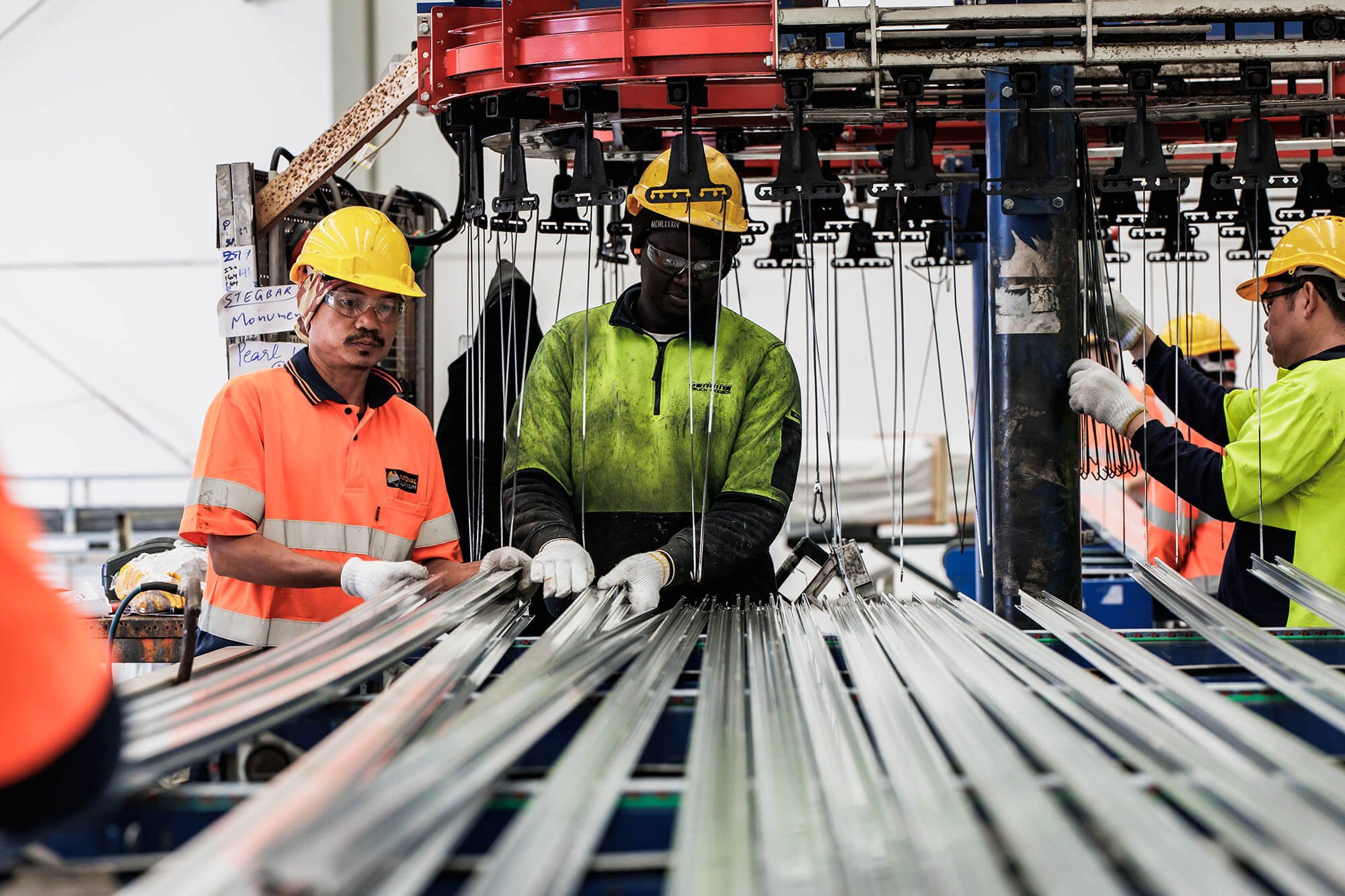 Two men in hi-vis outfits and hardhats working in an aluminium factory.