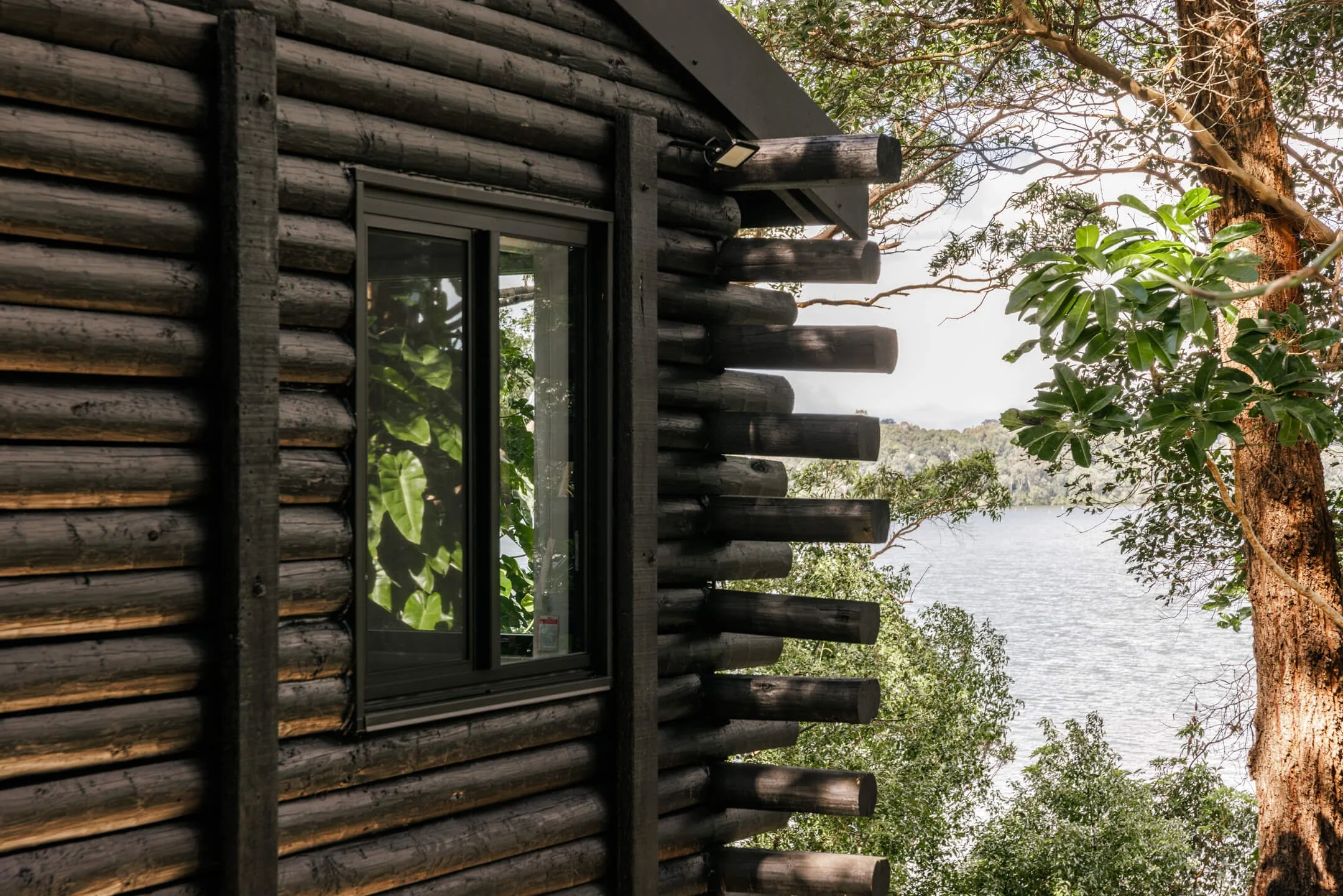 A modern wooden cabin with Bradnam's windows, overlooking a body of water with hills in the distance.