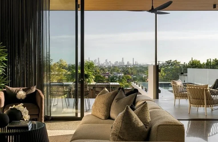 A modern lounge room with open glass sliding doors overlooking the city skyline in the distance.