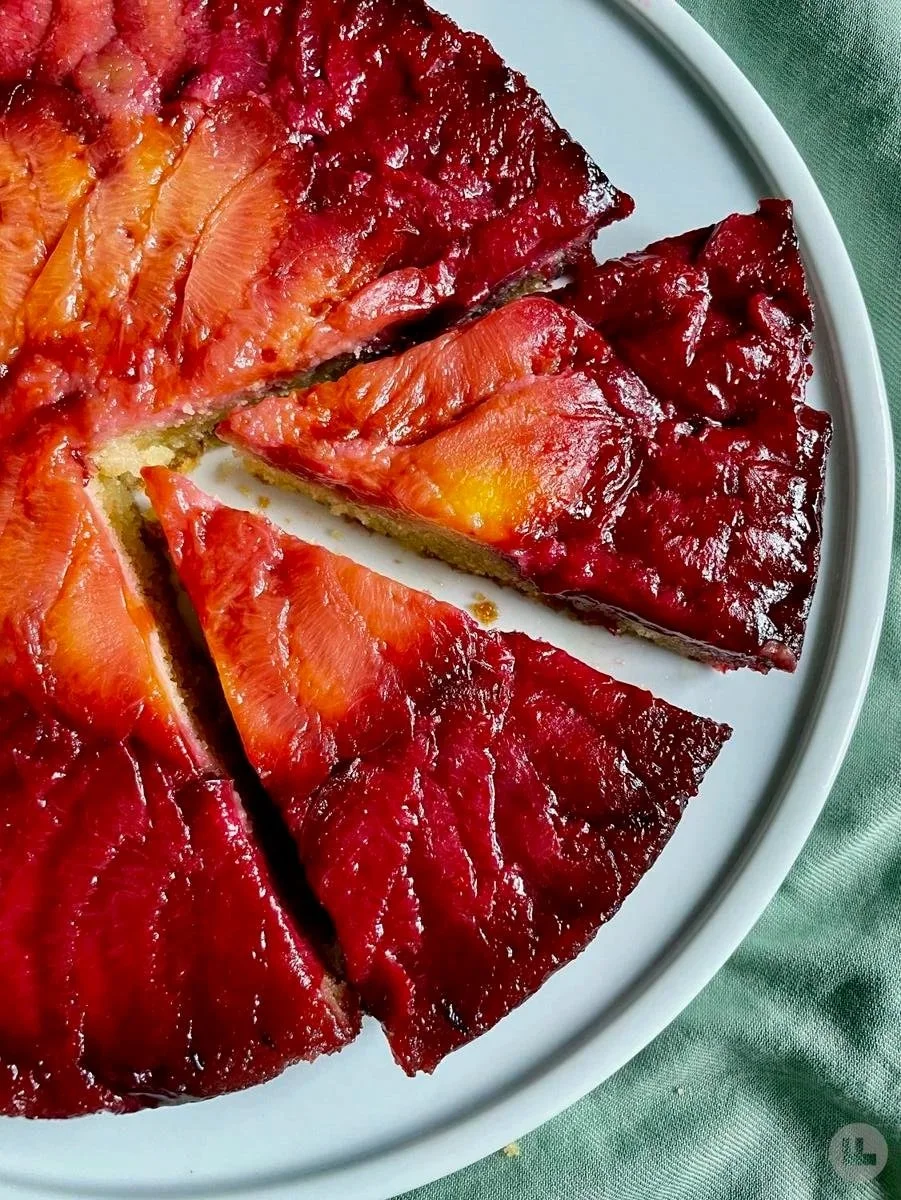 Strawberry and raspberry cheesecake with fresh strawberries and a raspberry topping on a white plate, cake has a graham cracker crust, set on a green tablecloth.