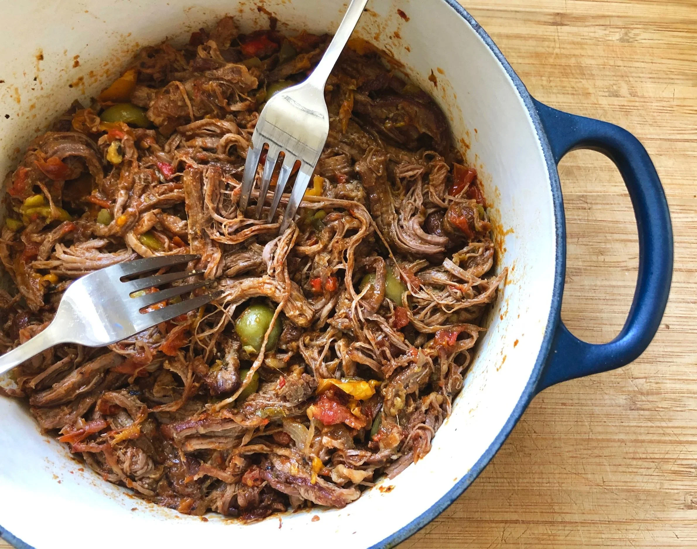 Shredded beef with vegetables in a white and blue cast iron skillet on a wooden surface.