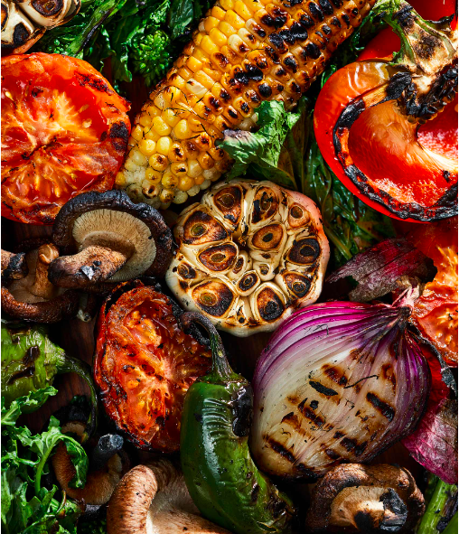 Grilled vegetables including corn on the cob, tomatoes, green peppers, red onion, mushrooms, and garlic.