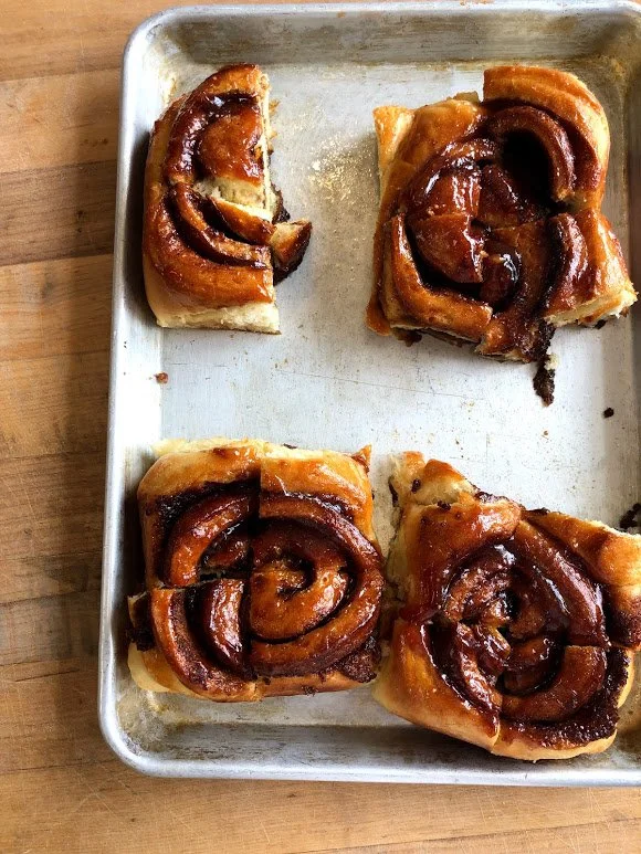 Four cinnamon rolls with icing on a baking sheet.