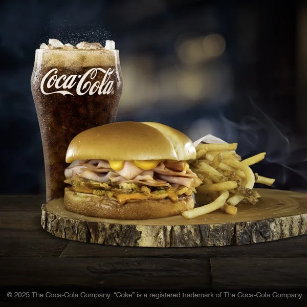 A cheeseburger with fries, a Coca-Cola soda with ice, on a wooden serving board.