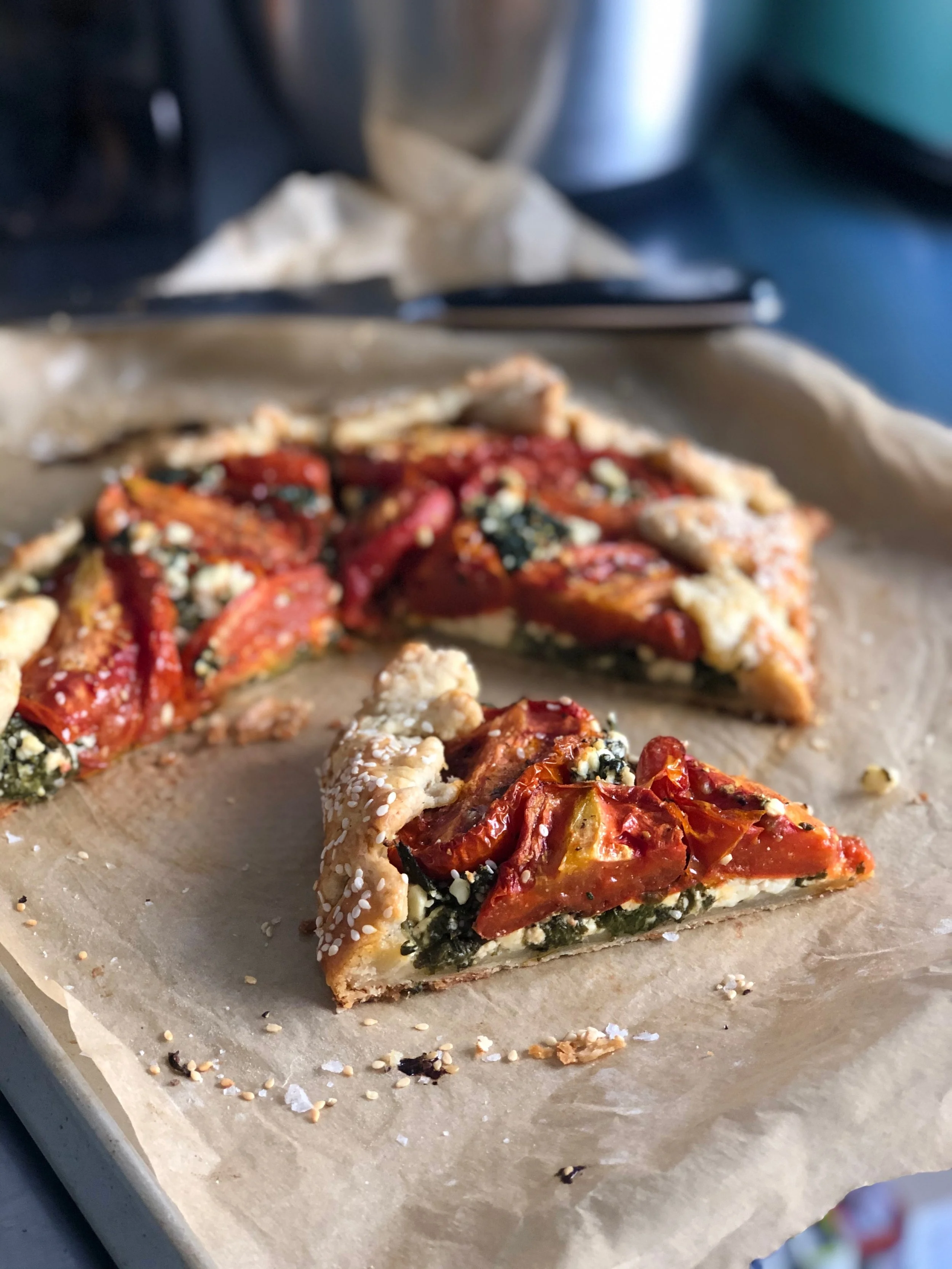 A slice of vegetable tart with red peppers, spinach, and cheese on a parchment-lined baking sheet.