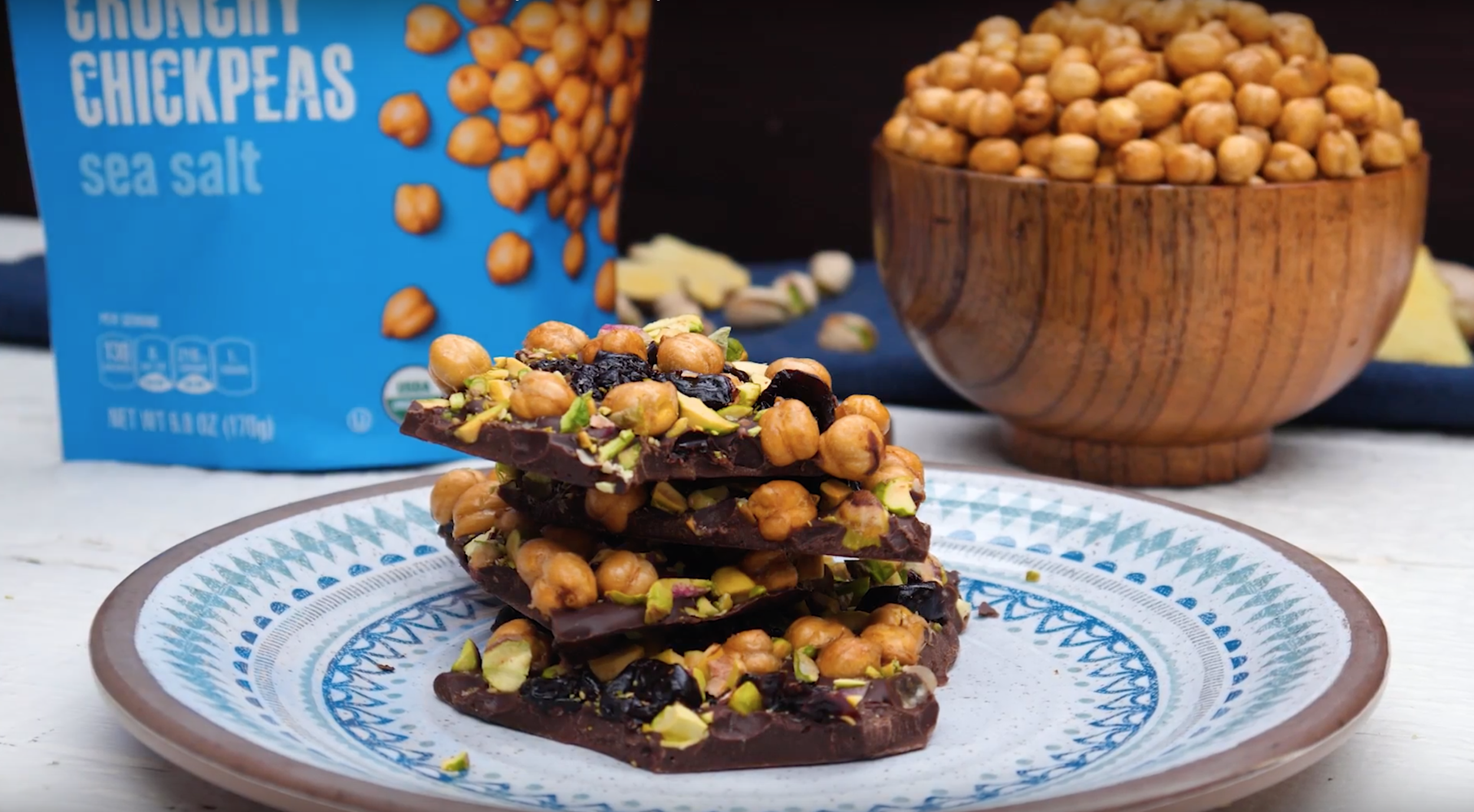 Stacked chocolate bark topped with chickpeas and chopped pistachios on a decorative plate.